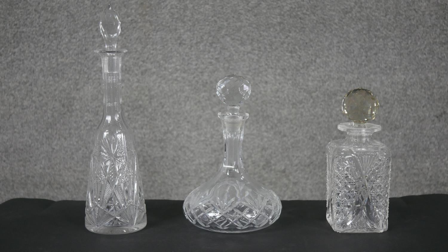 Three cut crystal decanters. One rectangular with a faceted ball stopper and the other two with