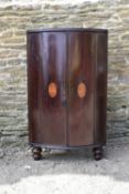 A Georgian mahogany bow fronted floor standing corner cabinet with ebonised top and inlaid fan