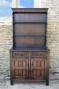 A mid century oak Jacobean style dresser with upper open plate rack above cupboards and drawers on