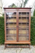 An early 20th century oak library bookcase with glazed panel doors enclosing book shelves on