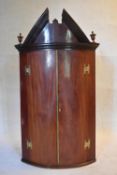A Georgian mahogany bowfronted hanging corner cabinet with arched pediment and urn finials and