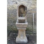 A weathered cast reconstituted stone lion mask alcove fountain on pedestal base. H.163 W.51 D.55cm