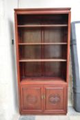 A Chinese teak floor standing open bookcase with carved character mark panel doors to the base. H.