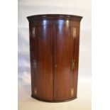 A Georgian mahogany bow fronted hanging corner cabinet with original brass work. H.118 W.74 D.48cm