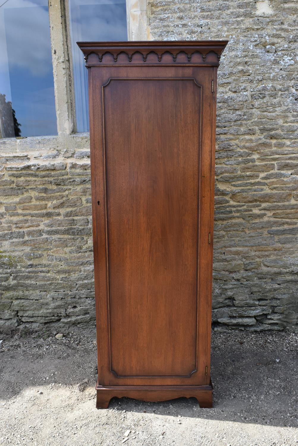 A Georgian style mahogany single wardrobe with panel door enclosing hanging section on shaped