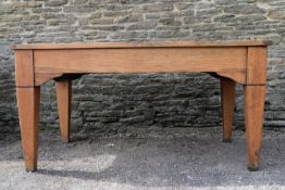 A mid century light oak library table with inset leather top and frieze drawer raised on square