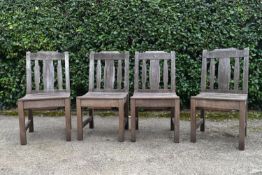 A set of four weathered teak garden chairs with carved back rails and slatted backs and seats on