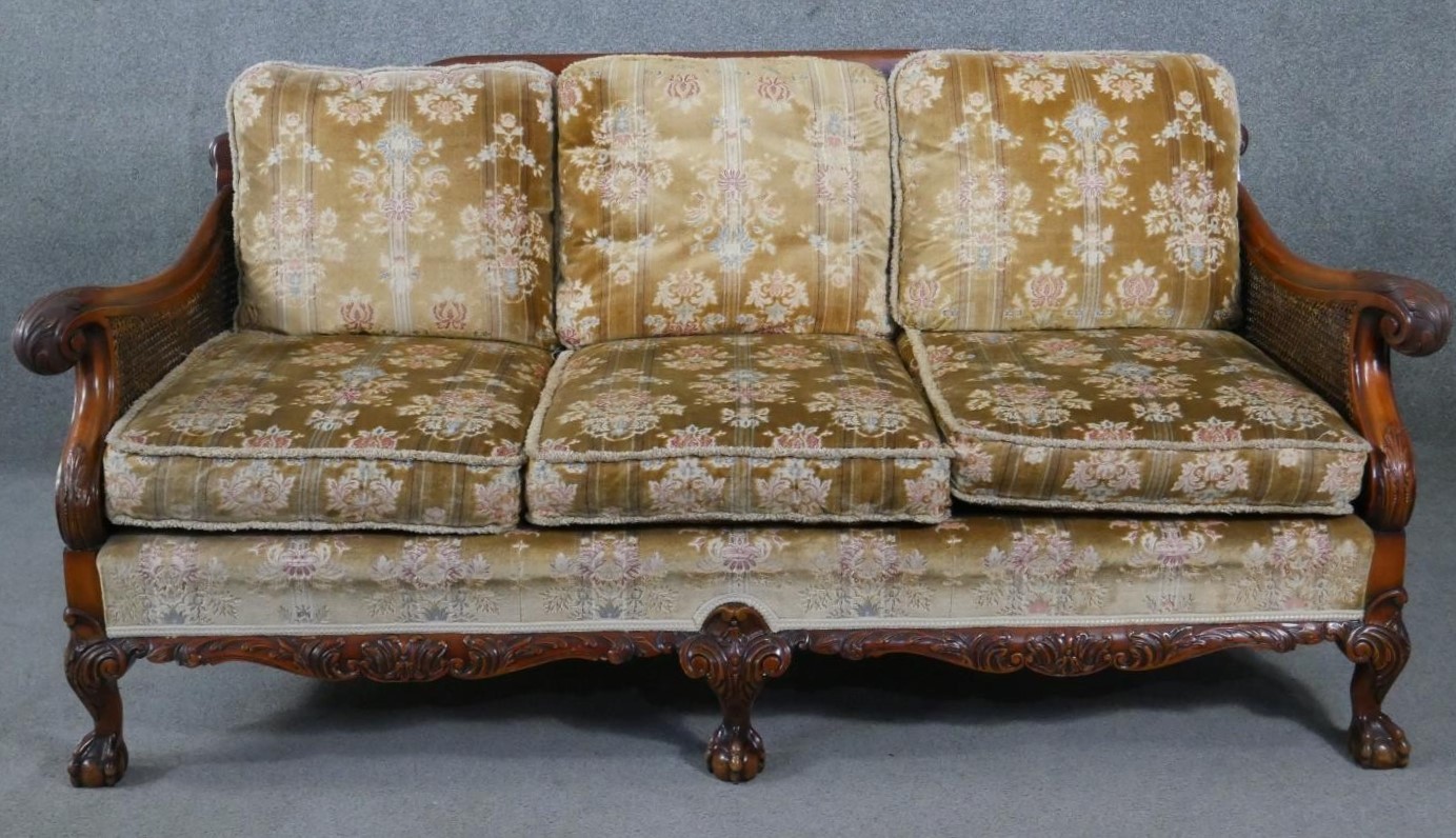 A mid century carved walnut three seater bergere sofa with double caned sides in cut floral