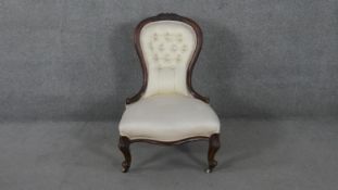A Victorian mahogany framed nursing chair with carved cresting and deep buttoned upholstery on
