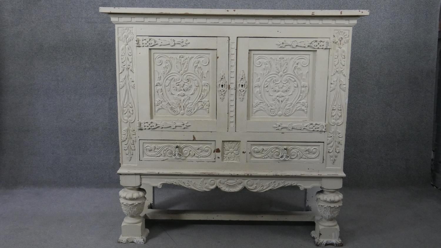 An early 20th century distressed painted 18th century style cabinet with all over carving on