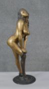 A large patinated brass erotic figure of a female rolling up a stocking. H.56 Diam.18cm