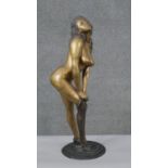 A large patinated brass erotic figure of a female rolling up a stocking. H.56 Diam.18cm