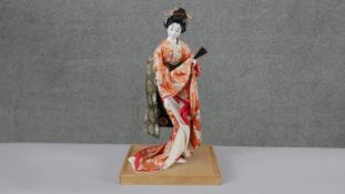 A vintage Japanese geisha girl doll on bamboo base. Dressed in a traditional silk kimono, with paper
