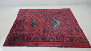 A Persian Loristan rug with double lozenge medallions on a claret ground within floral and