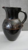 A large black and brown glaze art pottery jug with incised design. Impressed stamp to the base. H.38