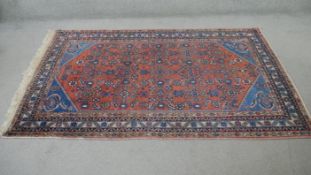 A Hamadan rug with repeating stylised floral motifs across the madder ground contained by