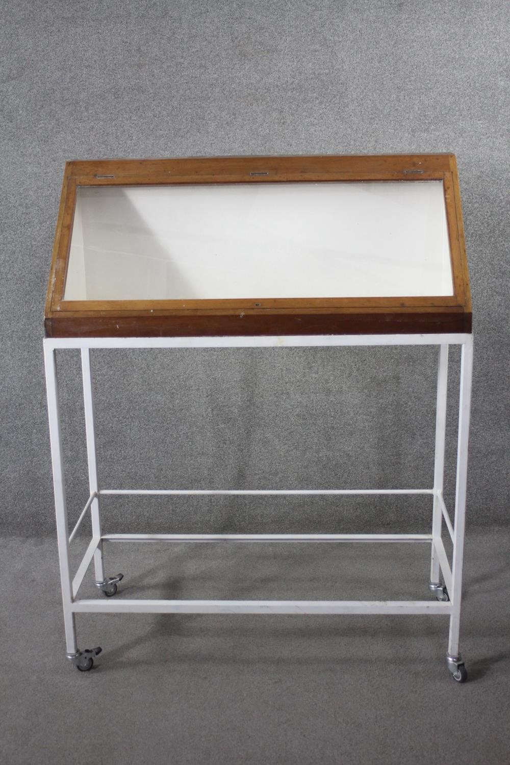 A lidded glazed mahogany display case on metal framed stand fitted with locking castors, from the