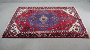 A Persian Hamadan rug with central stylised medallion on a madder field contained within