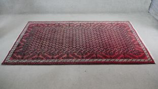 A Persian Meshed rug with repeating stylised flowerhead motifs across the field contained within