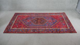 A Persian Hamadan rug with central hooked medallion on burgundy ground within foliate serrated