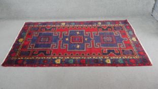 A Persian Hamadan rug with repeating central hooked medallions on a burgundy field within multiple