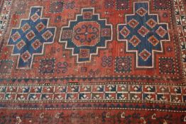 A Kurdish rug with central geometric medallions on a burgundy ground within stylised floral borders.