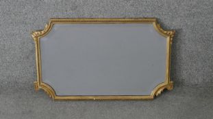 An early 20th century wall mirror with shaped bevelled plate in giltwood and gesso frame with beaded