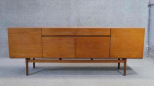 A vintage teak sideboard with an arrangement of drawers and cupboards on shaped stretchered tapering