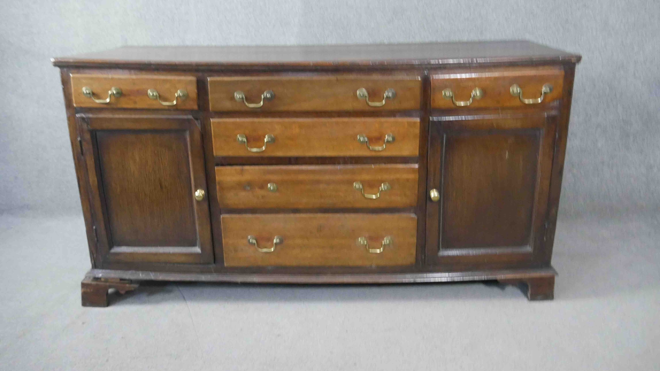 A Georgian country oak dresser base fitted with central drawers with brass swan neck handles flanked