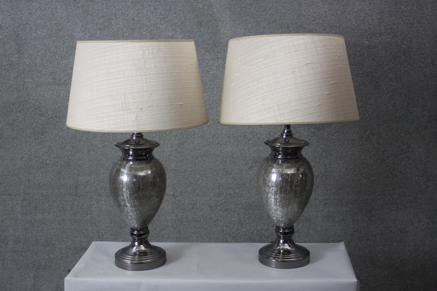 A pair of crackle mirrored grey glass urn design table lamps with cream shades. H.74 Diameter 18 cm.