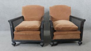 A pair of early 20th century mahogany framed bergere armchairs with carved arms on fluted bun feet.