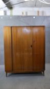 A vintage teak Austinsuite fitted wardrobe with central sliding tambour door on splay supports. H.
