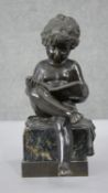 A 19th century bronze figure of a young child reading a book, mounted on a green marble base.