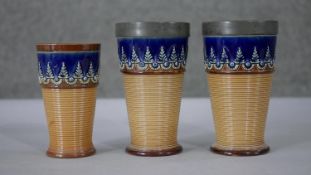 Three Doulton Lambeth glazed ceramic foliate design beakers. Two the same size with pewter rims