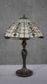 A vintage Tiffany style leaded stained glass table lamp with bronze effect foliate design base. H.60