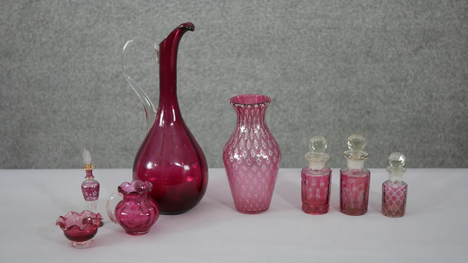 A collection of cranberry glass. Including an art glass water jug, a fishnet pattern golf foil art