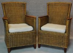 A pair of rattan conservatory armchairs with teak elbow rests and drop in squab seats. H.91cm