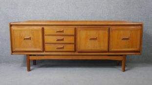 A mid century vintage teak sideboard with drawers flanked by cupboards on stretchered shaped