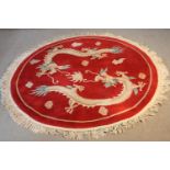 A Chinese woollen rug with chasing dragons on a burgundy ground. Dia. 160cm.