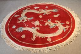 A Chinese woollen rug with chasing dragons on a burgundy ground. Dia. 160cm.