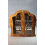 An Art Deco walnut cloud shaped display cabinet with sunray astragal glazed doors on plinth base.