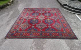 An Eastern carpet with repeating floral medallions across a burgundy field within foliate multiple