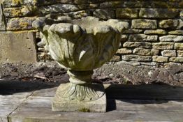 A weathered reconstited stone garden urn of scrolling acanthus leaf form on a pedestal base.