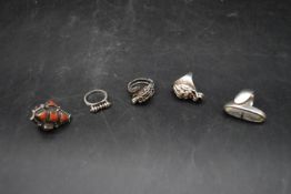 A collection of five silver rings. Including a silver dress ring inlaid with coral, a Chinese silver