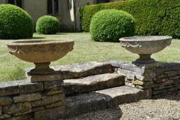 A pair of weathered reconstituted stone two section garden urns with swag relief decoration on