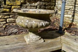 A weathered reconstituted stone garden urn with gadrooned sides on a pedestal base.