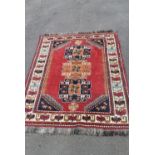 A hand woven Persian Qashgai rug with triple lotus leaf medallions on a burgundy ground within