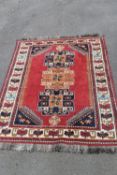 A hand woven Persian Qashgai rug with triple lotus leaf medallions on a burgundy ground within