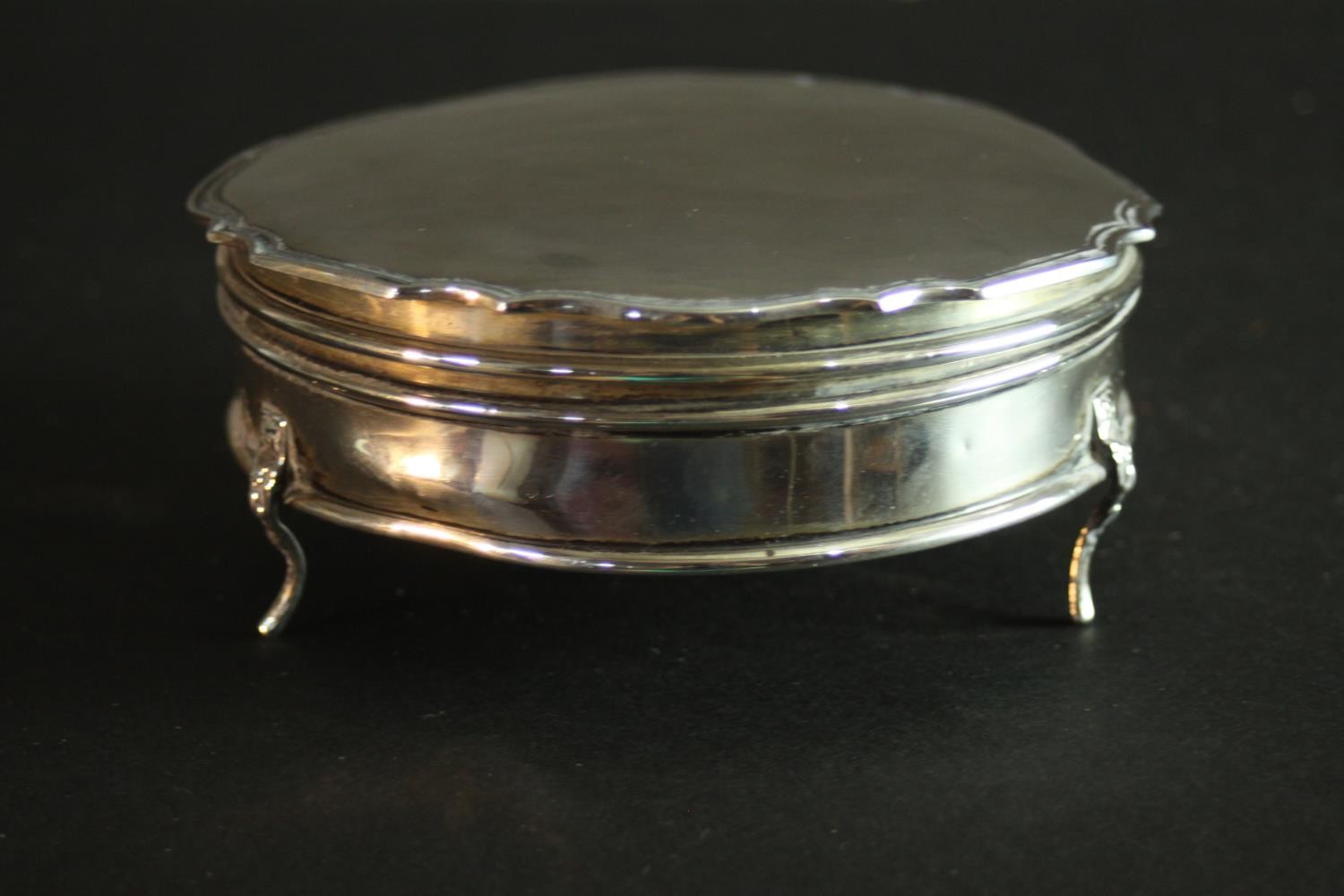 An 1920's hinged lidded silver box with scalloped edge and on tripod feet. Gilded interior and