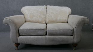 A two seater Victorian style scroll arm sofa in floral upholstery on turned supports terminating